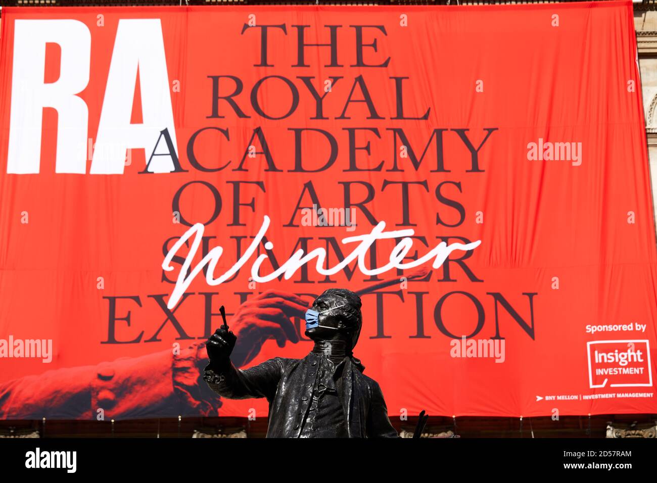 London, Großbritannien. - 5. Oktober 2020: Eine maskierte Statue vor einem Banner für die traditionelle Royal Academy Summer Exhibition, die wegen der Coronavirus-Pandemie bis Oktober verschoben wurde. Stockfoto