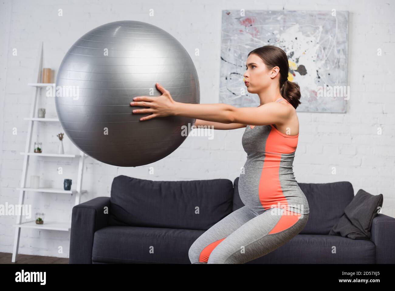 Brunette schwangere Frau Atmung während dabei hocken mit Fitness-Ball Im  Wohnzimmer Stockfotografie - Alamy