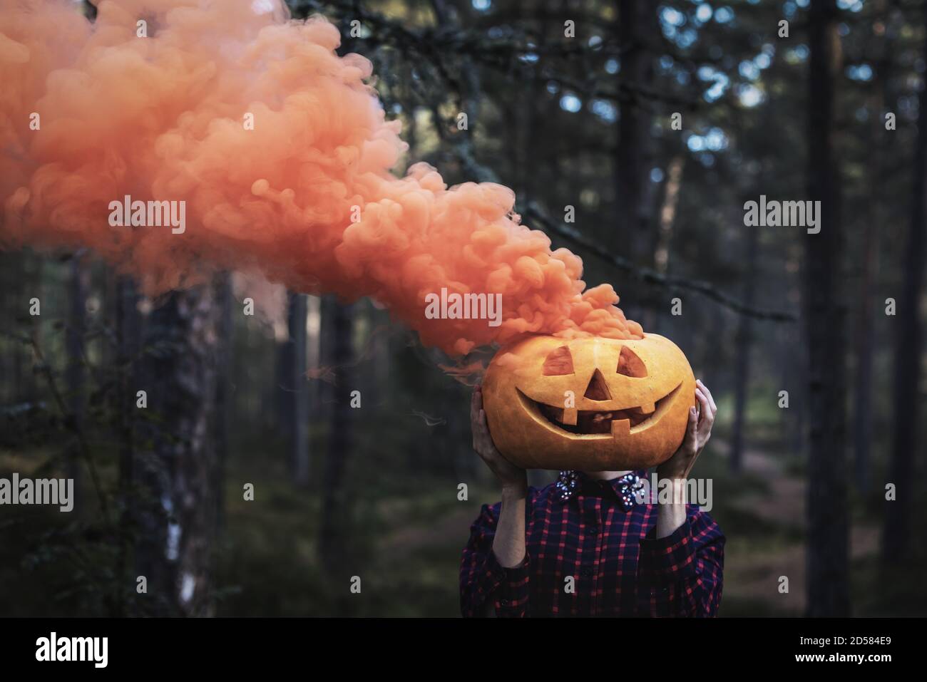 Frau hält geschnitzten halloween Kürbis mit orangenen Rauch vor Von ihrem Gesicht im Wald Stockfoto