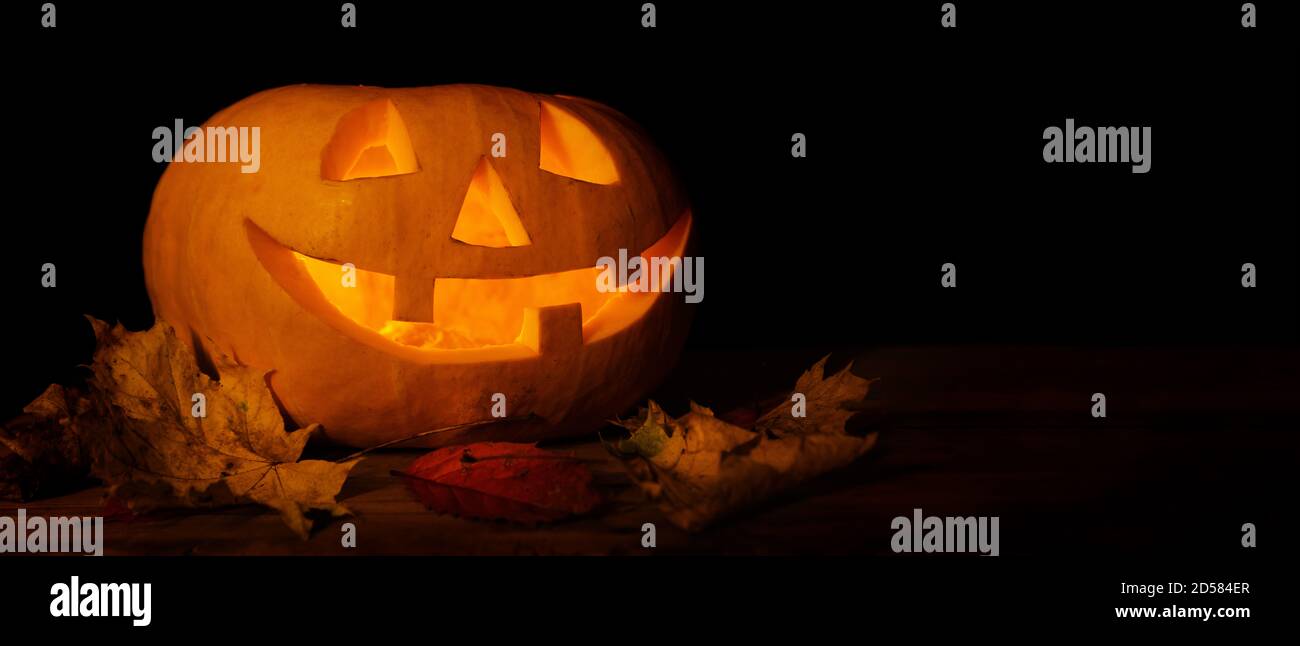 Glühender geschnitzter halloween Kürbis mit Herbstblättern auf dunklem Hintergrund. Banner-Kopierraum Stockfoto