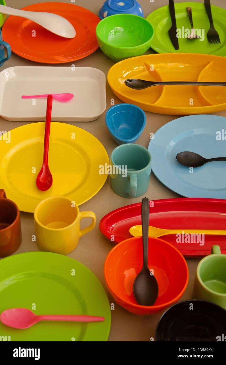 Kreative Komposition mit Melamin Crockery bestehend aus Tellern, bunten Schalen und Löffeln. Grauer Hintergrund. Innenaufnahme im Studio. Vertikal Stockfoto