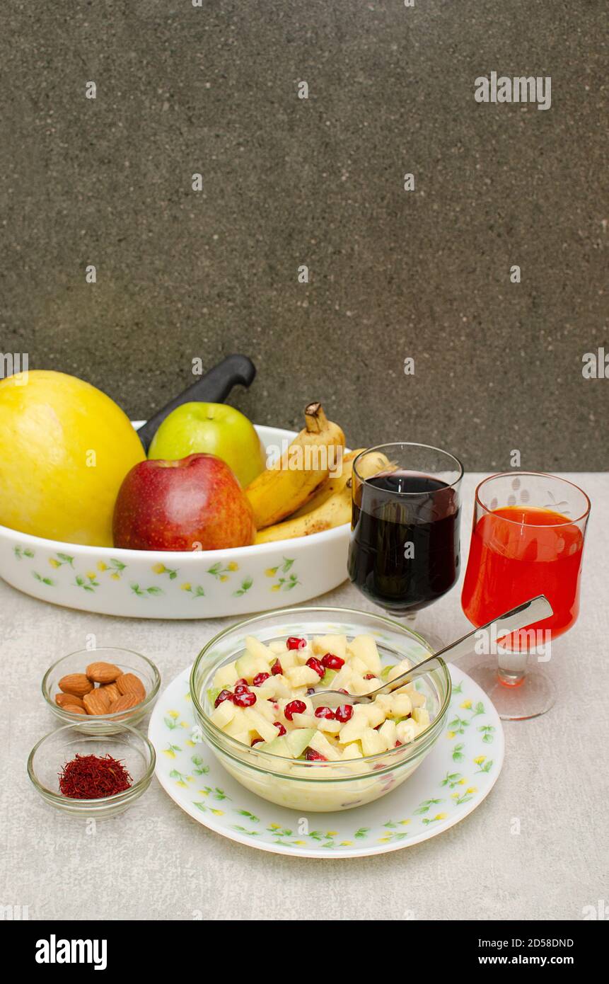 Obstschale mit Birne, rotem Apfel, grünem Apfel, Banane und Kanarienmelone auf einem Teller angeordnet. Schale mit Obstsalat, Mandel- und Safranschale. Glas Stockfoto