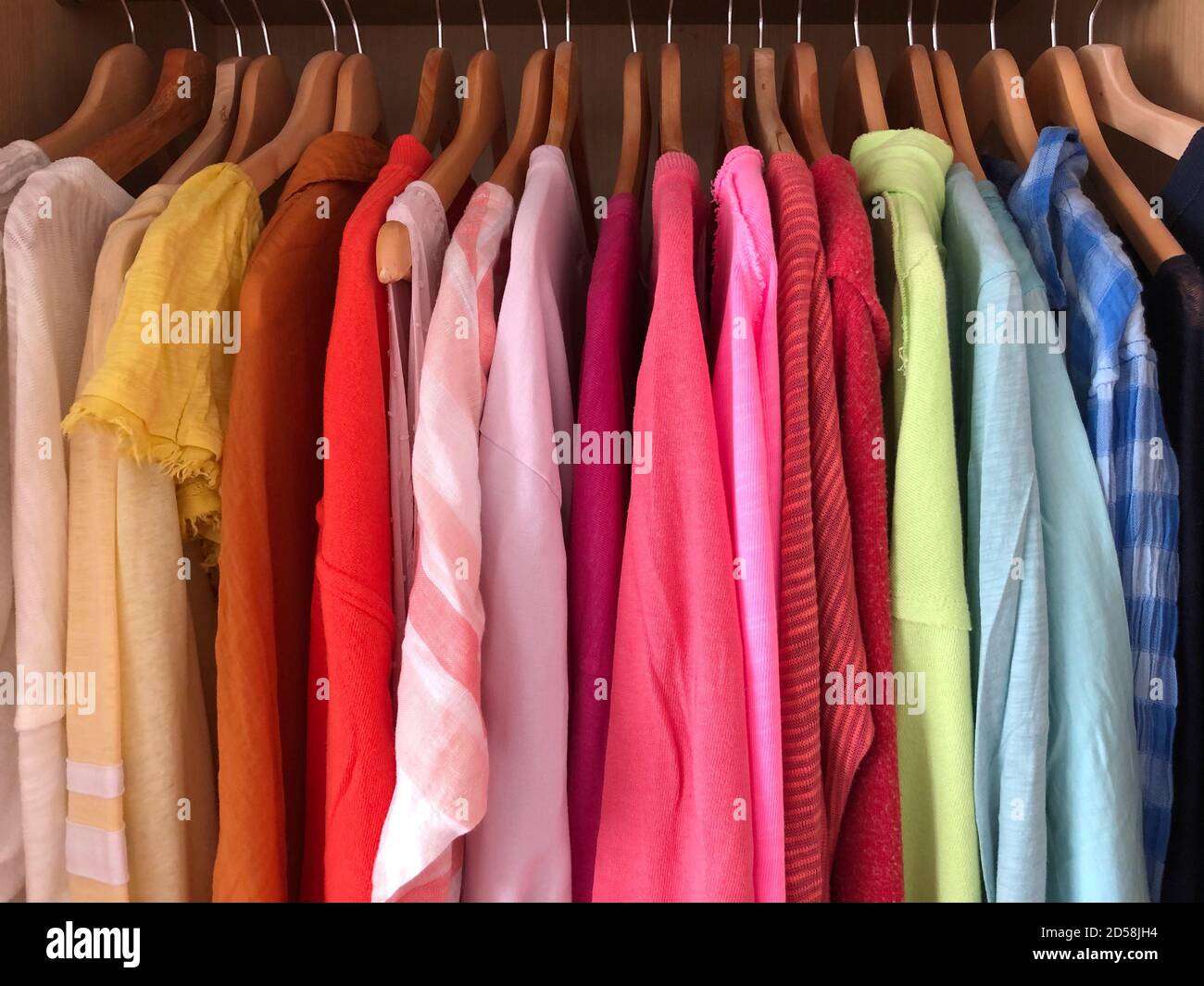 Regenbogenfarbene Tops hängen in einem Kleiderschrank Stockfoto
