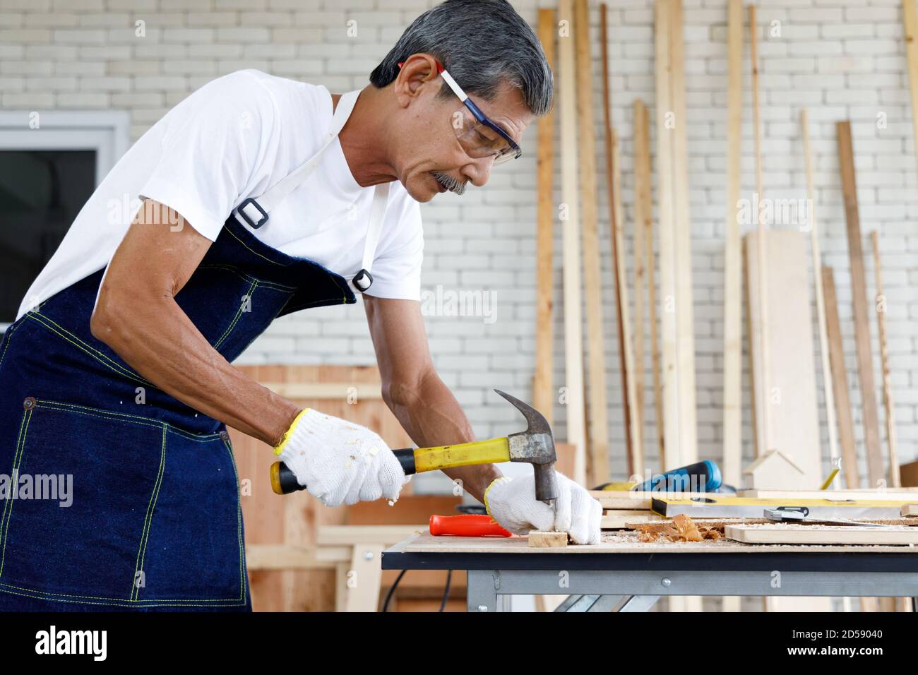 Asiatische Senior Mann Nagel Holzbrett in Schreinerei Werkstatt. Konzept Senioren Hobby nach dem Ruhestand. Stockfoto