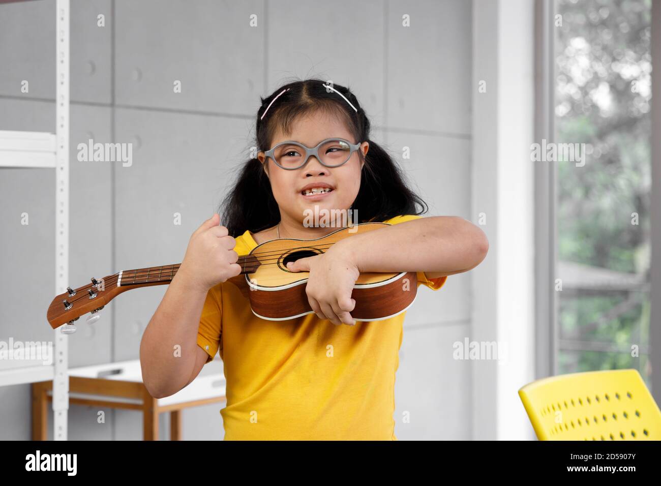 Glücklich asiatische Mädchen mit Down-Syndrom spielen Ukulele. Konzept deaktiviert Kind lernen. Stockfoto