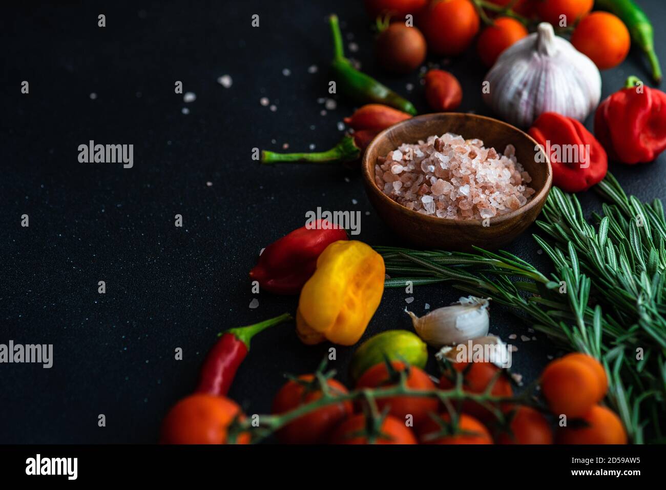 Schüssel mit rosa Himalaya-Steinsalz mit frischen Tomaten, Chili, Knoblauch und Rosmarin Stockfoto