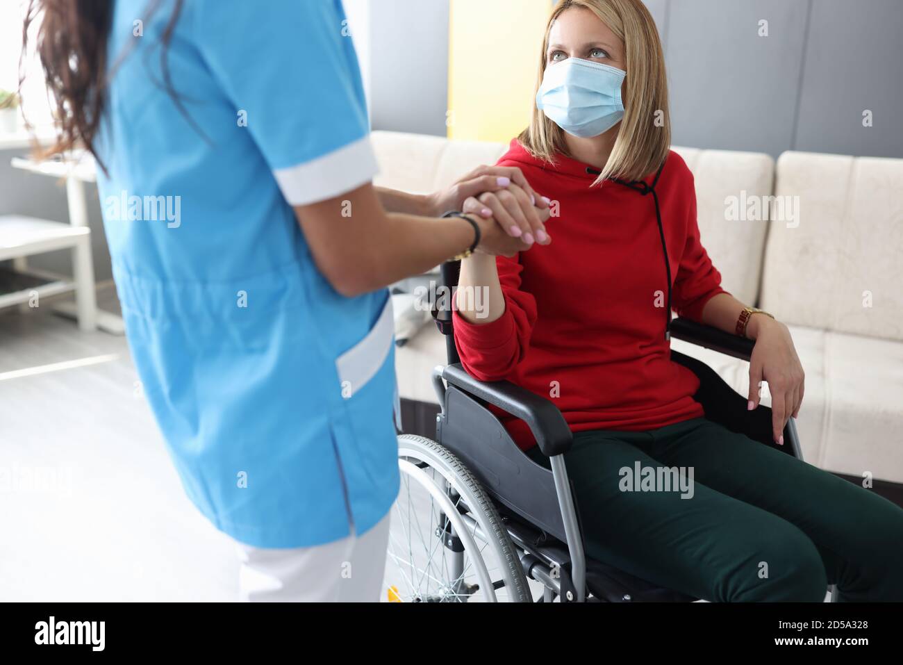 Arzt in Uniform hält die Hand der kranken jungen Frau in Rollstuhlporträt Stockfoto