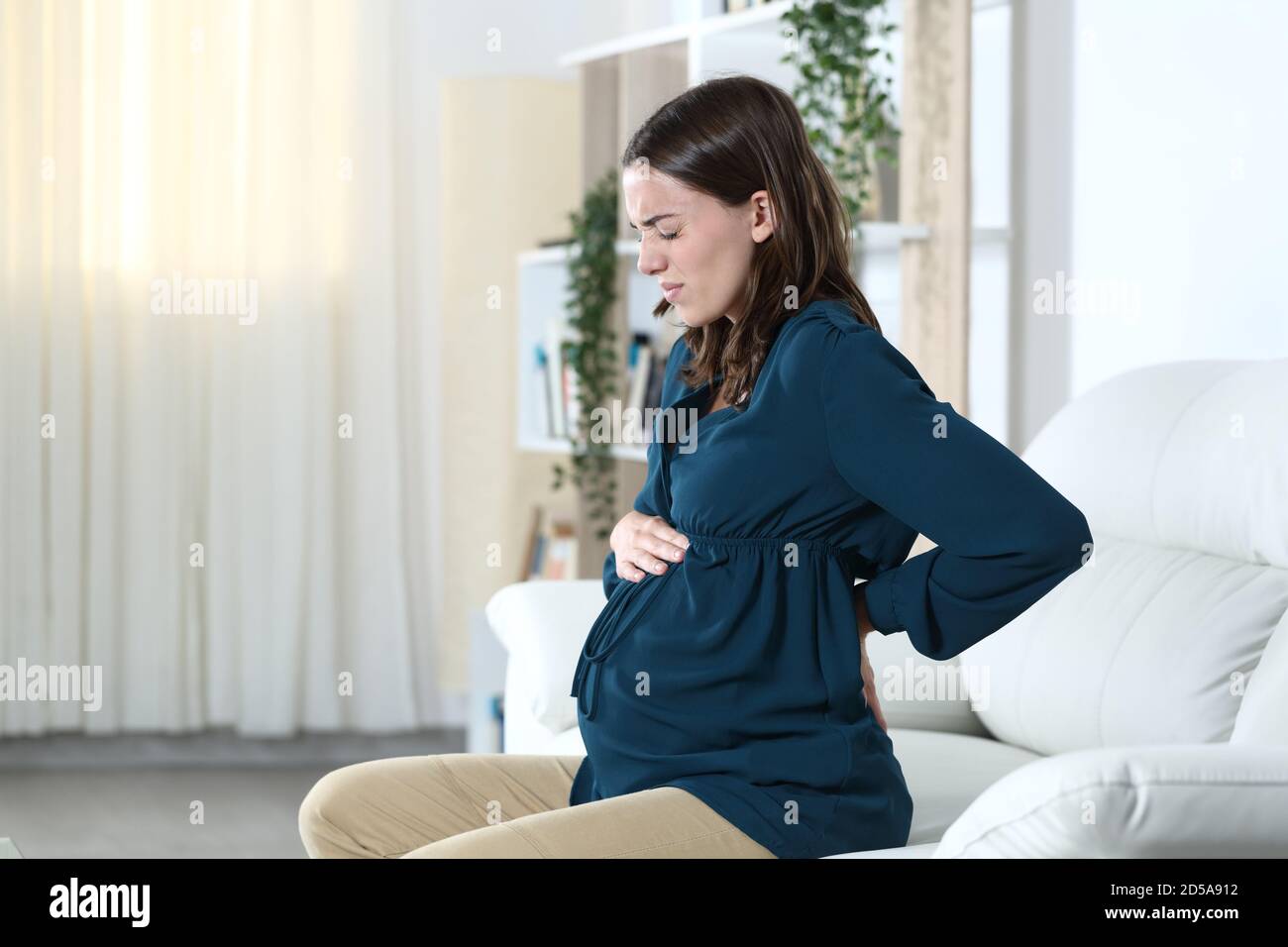 Schwangere Frau mit Rückenschmerzen beschwert sitzen auf einem Sofa Im Wohnzimmer zu Hause Stockfoto