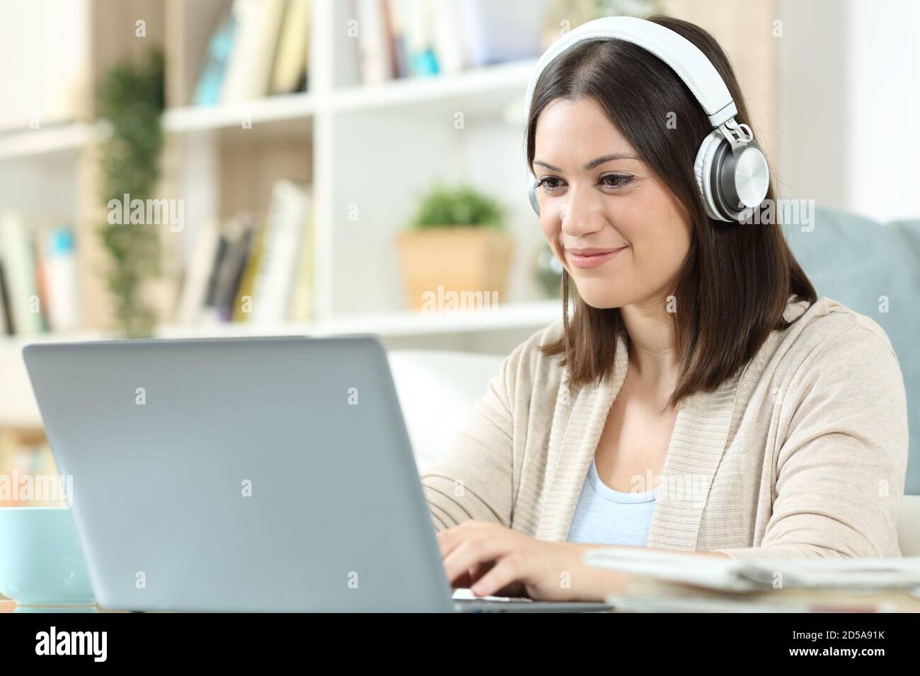 Frau mit Kopfhörern, die einen Laptop auf einem Schreibtisch sitzt Zu Hause Stockfoto