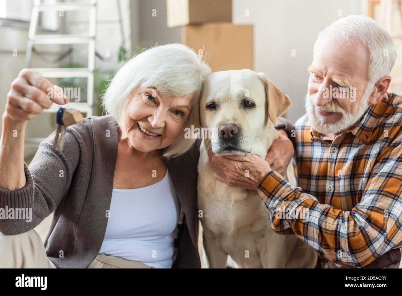 Senior Mann Streichelhund während Frau hält Schlüssel, bewegen Konzept Stockfoto