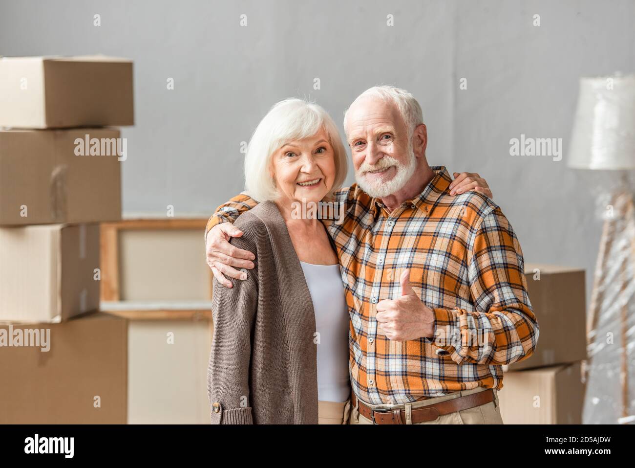 Ältere Paar umarmt und Mann zeigt dump up in neues Haus, Umzug Konzept Stockfoto