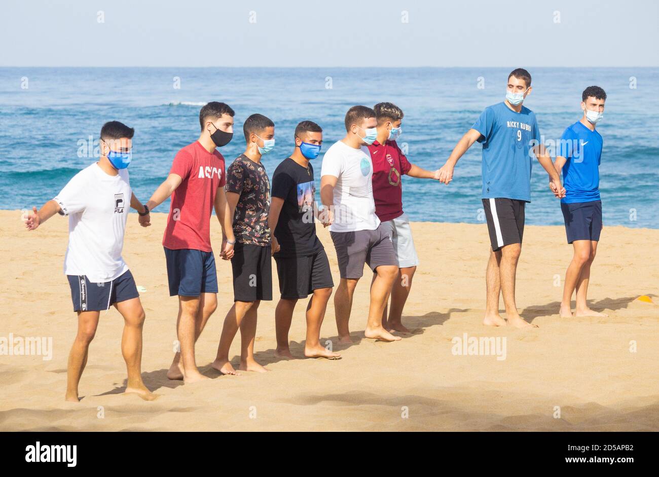 Las Palmas, Gran Canaria, Kanarische Inseln, Spanien. Oktober 2020. Studenten tragen Gesichtsbezüge spielen Mannschaftsspiele am Stadtstrand in Las Palmas für sich selbst, als die Temperaturen 35 Grad Celcius erreichen. Die Wirtschaft der Kanarischen Inseln leidet unter dem Mangel an Touristen aus dem Vereinigten Königreich. Obwohl sie eine der Provinzen Spaniens mit den geringsten Covid-Fällen sind, bleiben die Kanarischen Inseln wie auch der Rest Spaniens auf der Quarantäneliste des Vereinigten Königreichs. Kredit: Alan Dawson/Alamy Live Nachrichten. Stockfoto