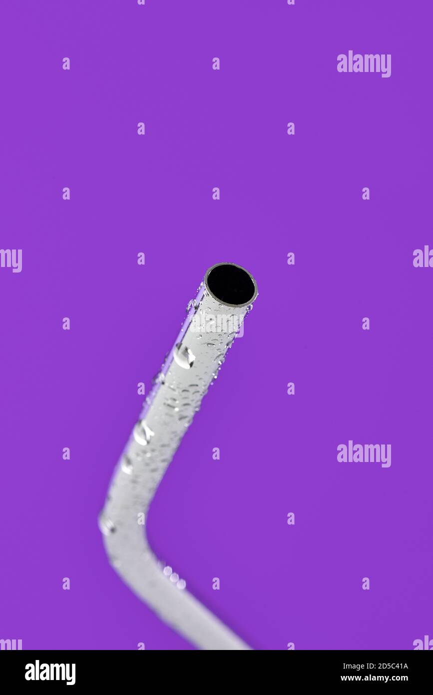 Nahaufnahme eines nassen wiederverwendbaren Trinkhalms aus Edelstahl Ein violetter Hintergrund Stockfoto
