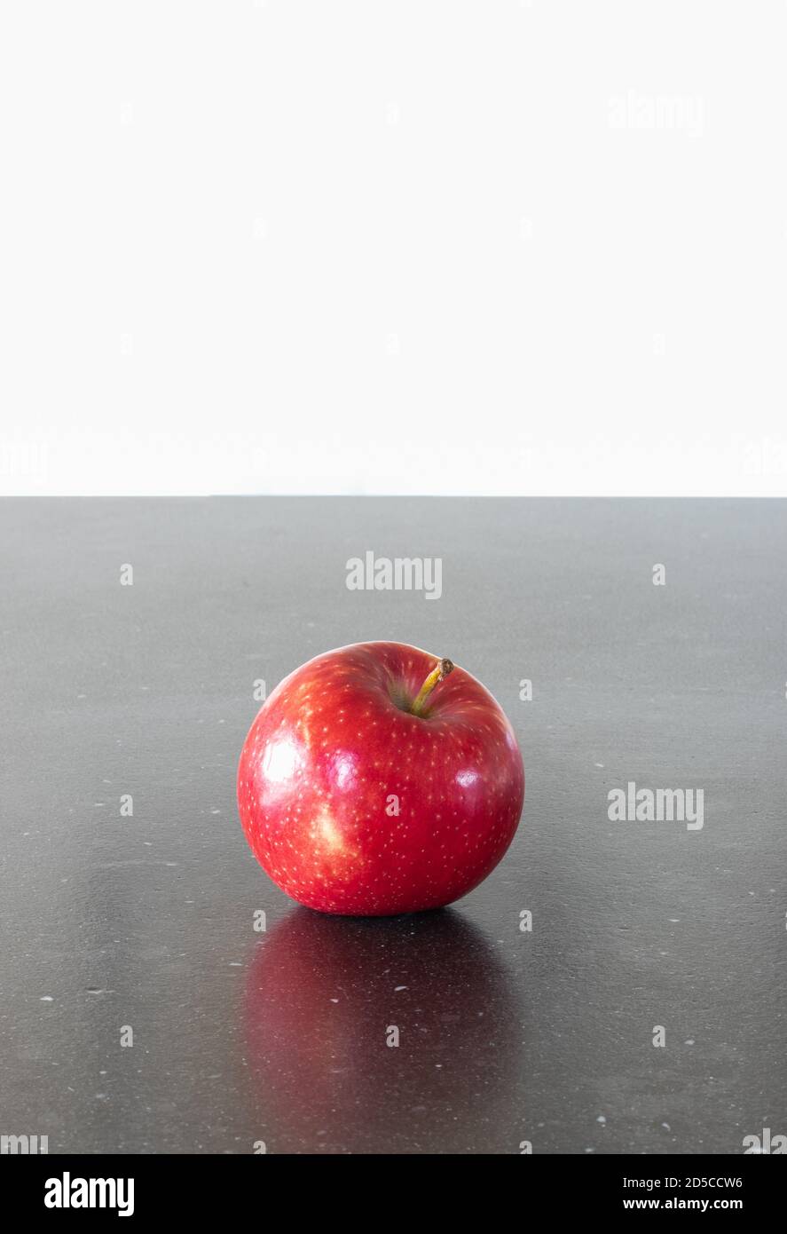 Ein Apfel am Tag hält den Arzt fern. Ein roter leckerer und glänzernder Apfel auf dunklem Hintergrund, Küchentischplatte. Gesunde Snacks und gesunde Ernährung Stockfoto