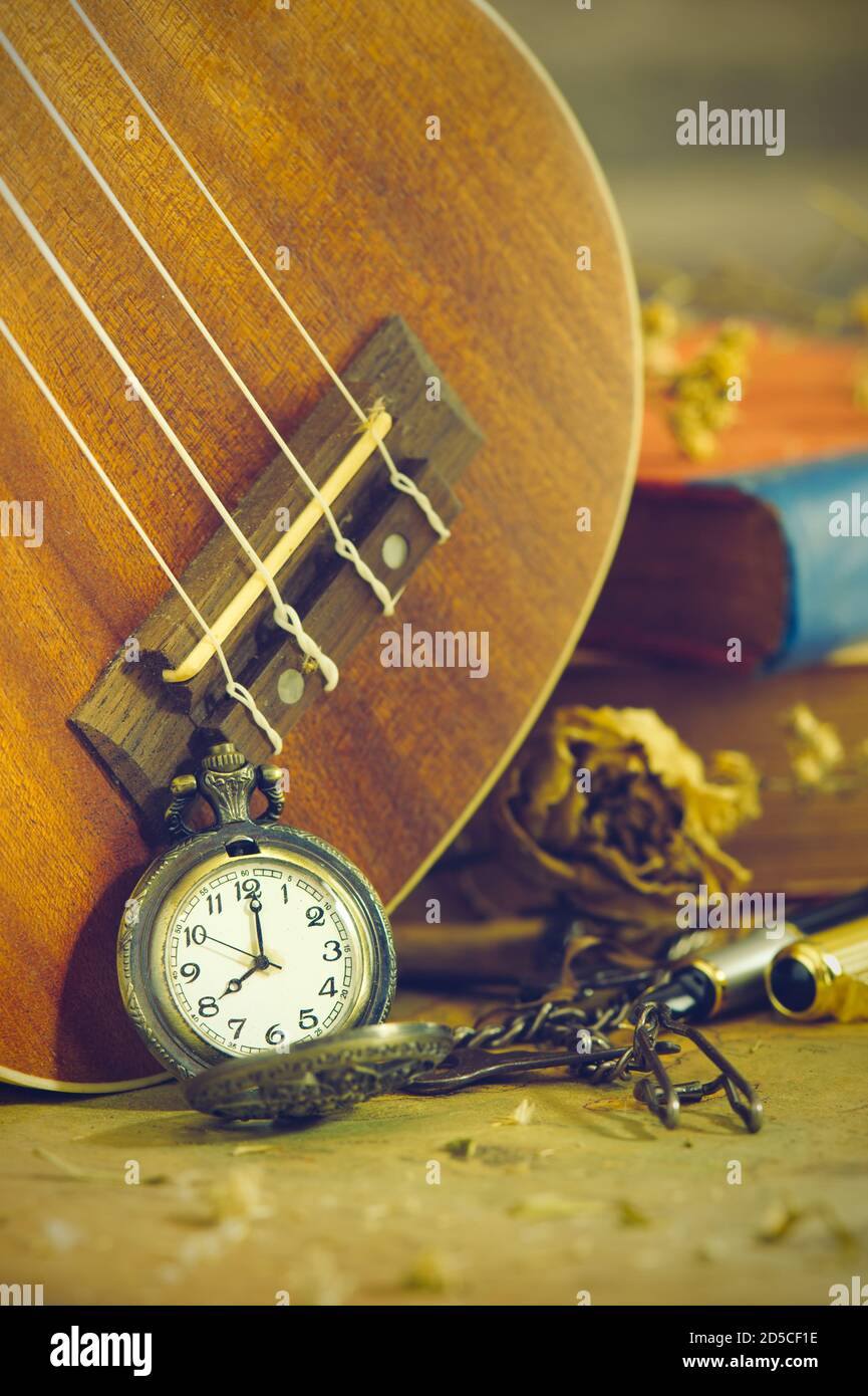 Eine antike Taschenuhr lehnte sich an eine Ukulele und ein altes Buch mit Vintage-Karte und Messingstift auf Holztisch platziert. Nahaufnahme und Kopie Platz für Text. Stockfoto