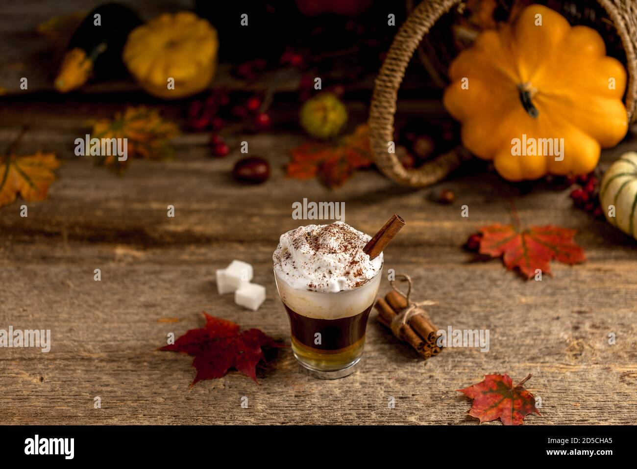 Kürbisgewürz Latte mit Zimtpulver und köstlichen Aromen auf Der alte texturierte Holztisch mit bunten trockenen Blättern und Kürbisse Stockfoto