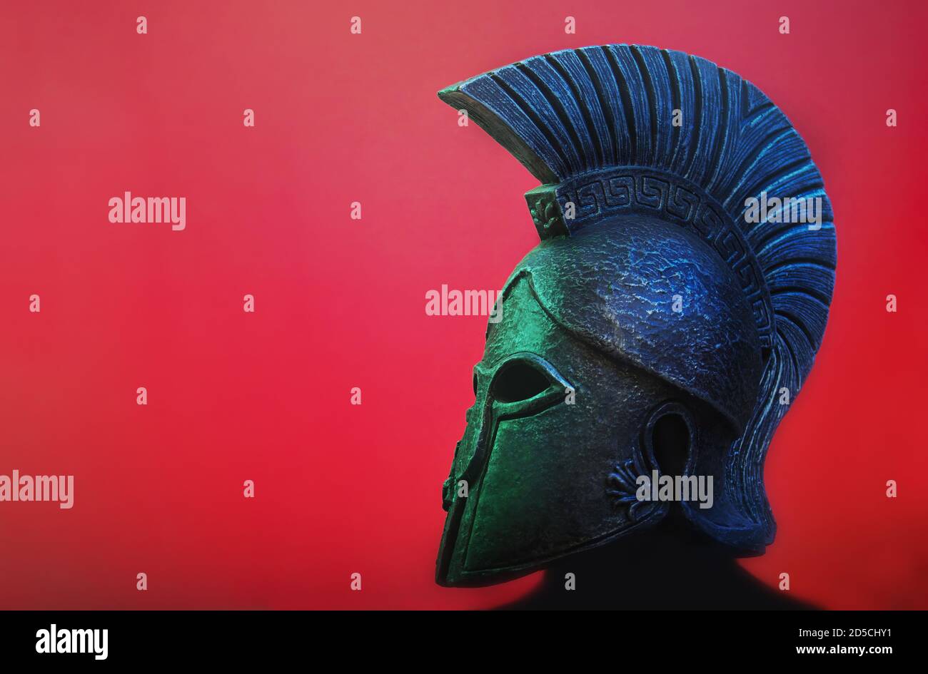 Antiker spartanischer (griechischer) Krieger-Helm auf rotem Hintergrund mit Texthintergrund. Geeignet für TV-Dokumentationen, Geschichte Informationen etc. Stockfoto