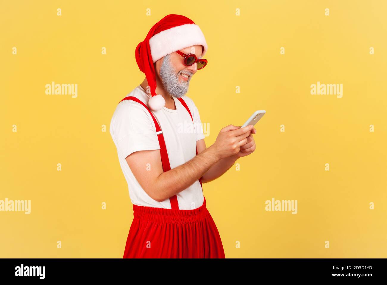 Profilportrait glücklicher Mann in Sonnenbrille und weihnachtsmann Kostüm chatten auf Smartphone, kein Internet-Verkehr in Boten. Innenaufnahmen im Studio Isolate Stockfoto