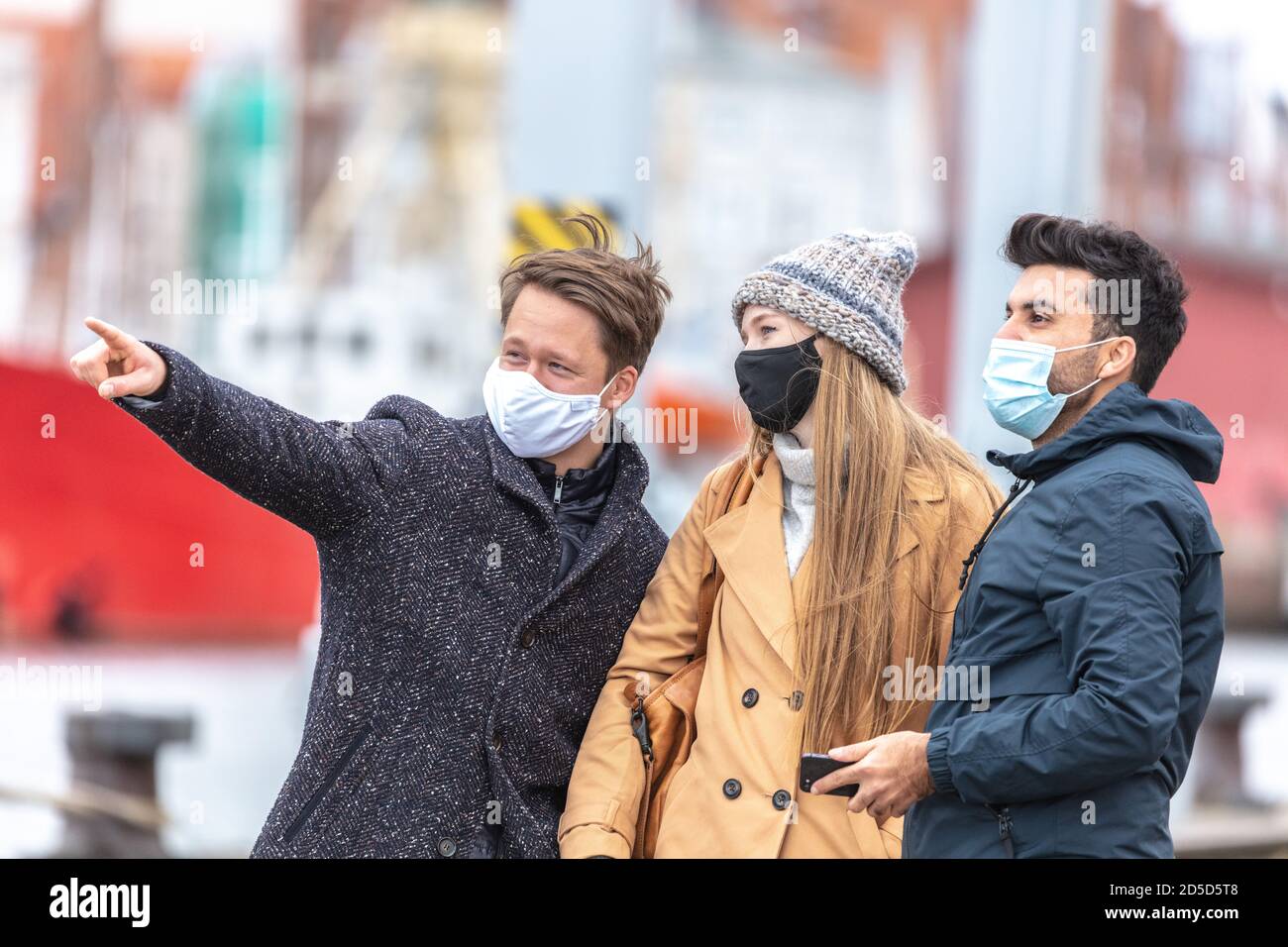 Zwei Männer und eine Frau in Corona-Zeit, mit alltäglichen Masken, in der kalten Jahreszeit in der Stadt unterwegs. Stockfoto