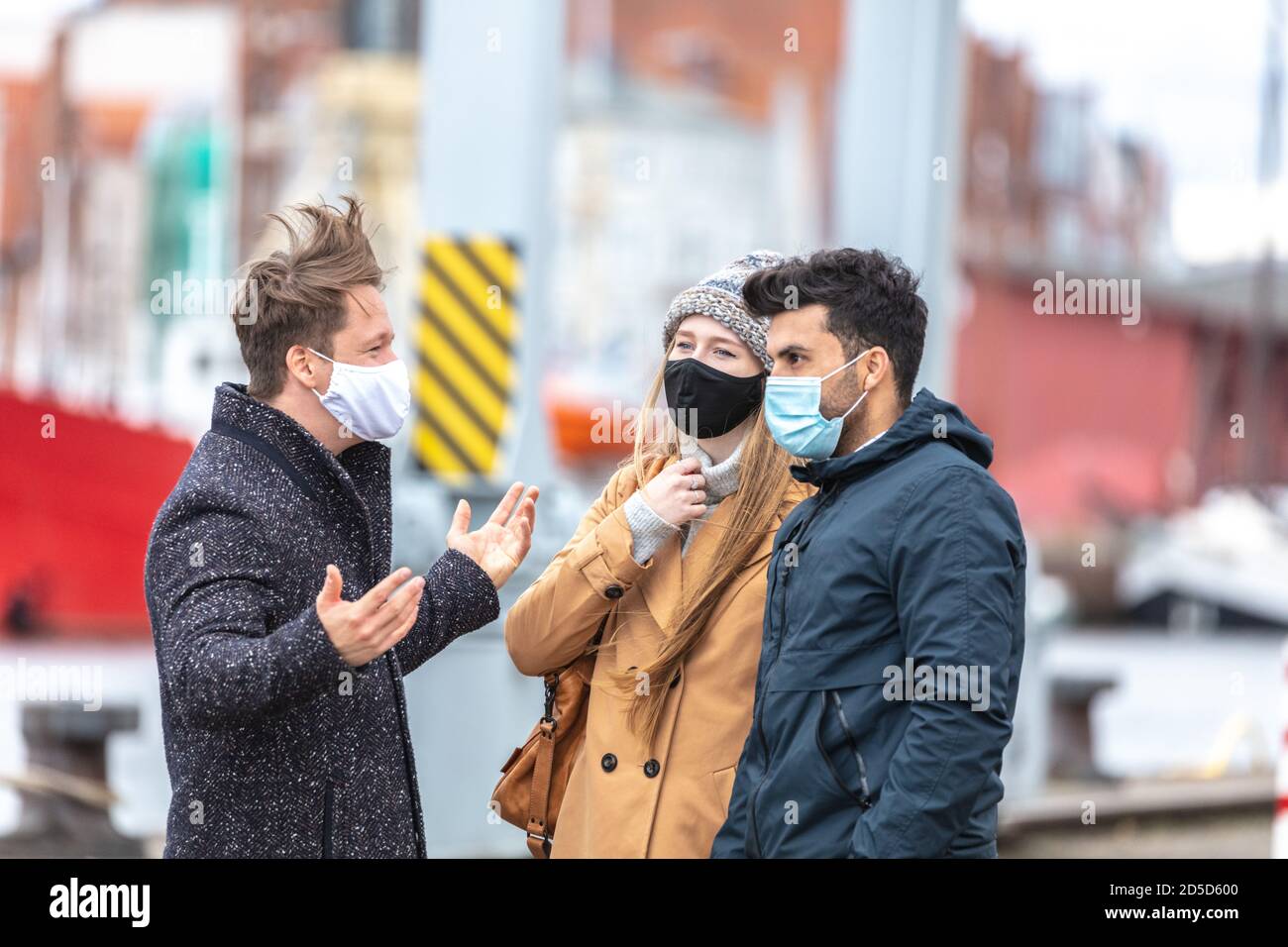 Zwei Männer und eine Frau in Corona-Zeit, mit alltäglichen Masken, in der kalten Jahreszeit in der Stadt unterwegs. Stockfoto