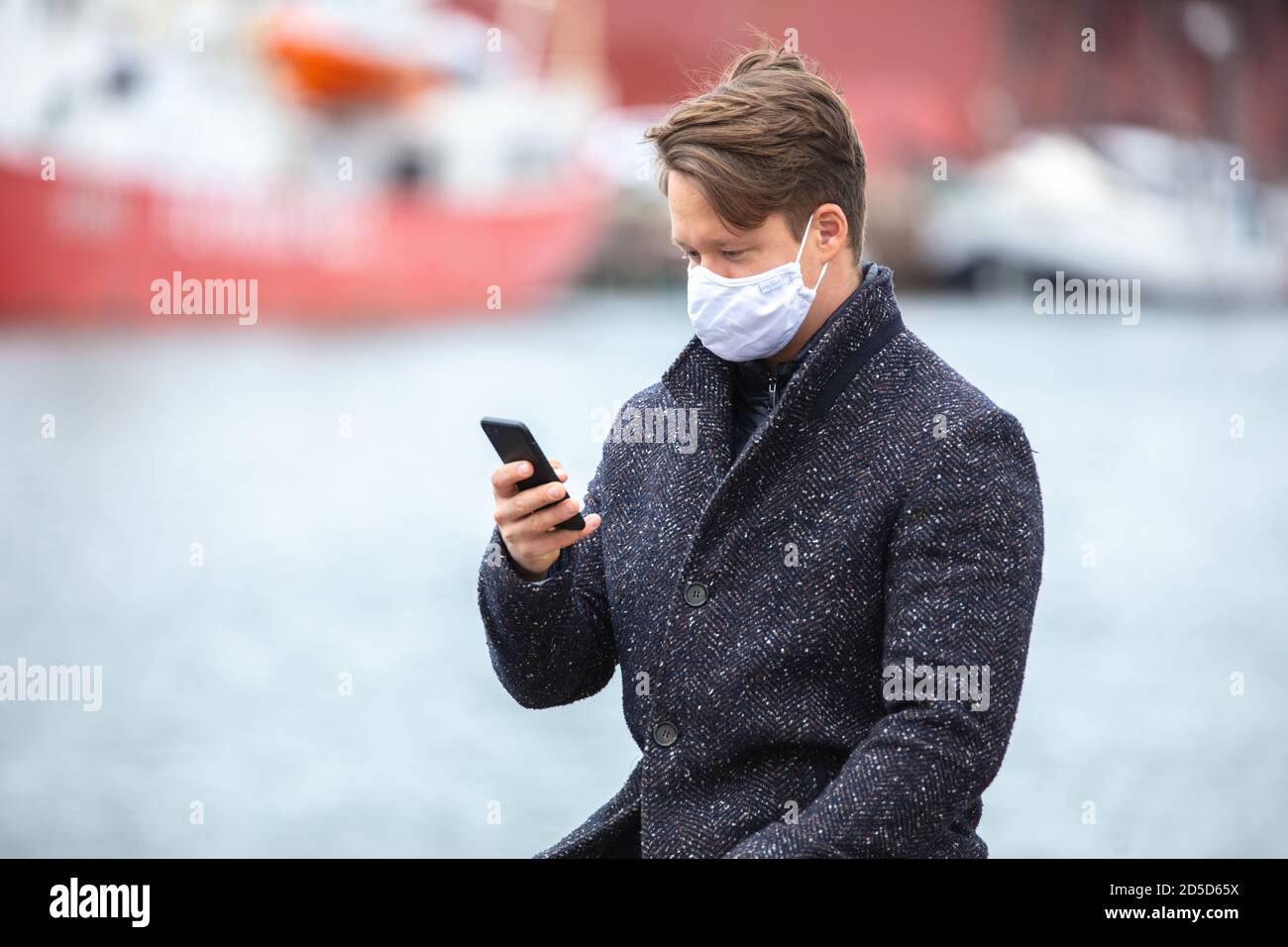 Junger Mann Coronazit, mit Alltagsmasken und Smartphone, in der kalten Jahreszeit in der Stadt unterwegs. Stockfoto