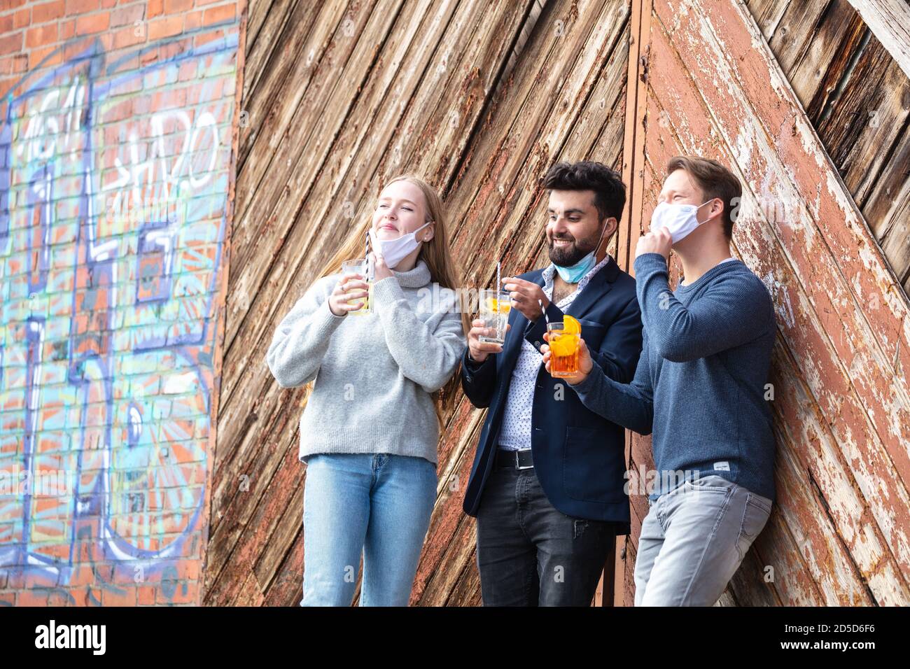Gruppe junger Menschen zur Cornazit mit Alltagsmaske, Freizeit in der Stadt mit Maske. Stehen mit Getränke im freien. Stockfoto