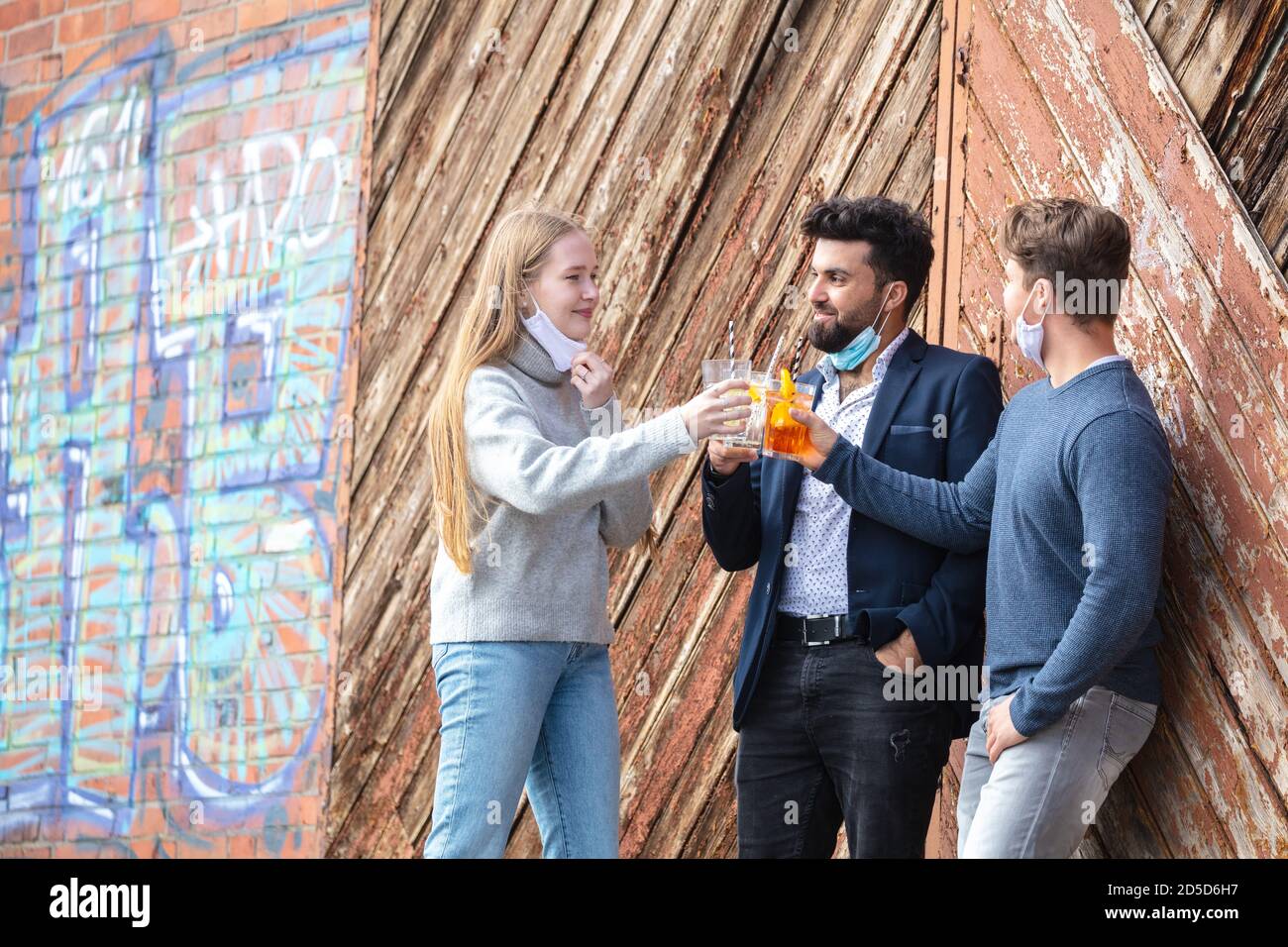 Gruppe junger Menschen zur Cornazit mit Alltagsmaske, Freizeit in der Stadt mit Maske. Stehen mit Getränke im freien. Stockfoto