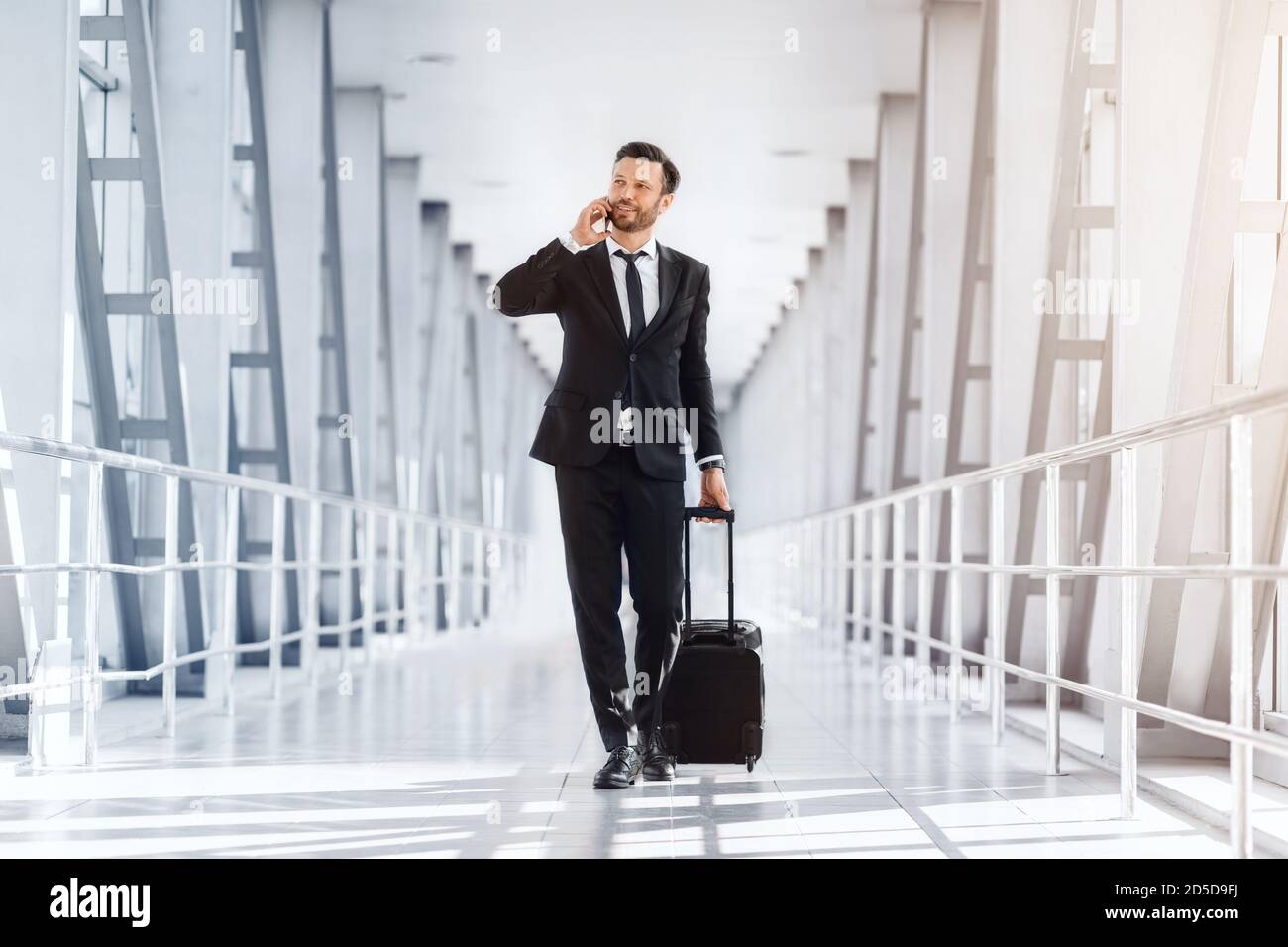 Wohlhabender gutaussehender Unternehmer mit Koffer zu Fuß vom Flughafen Stockfoto