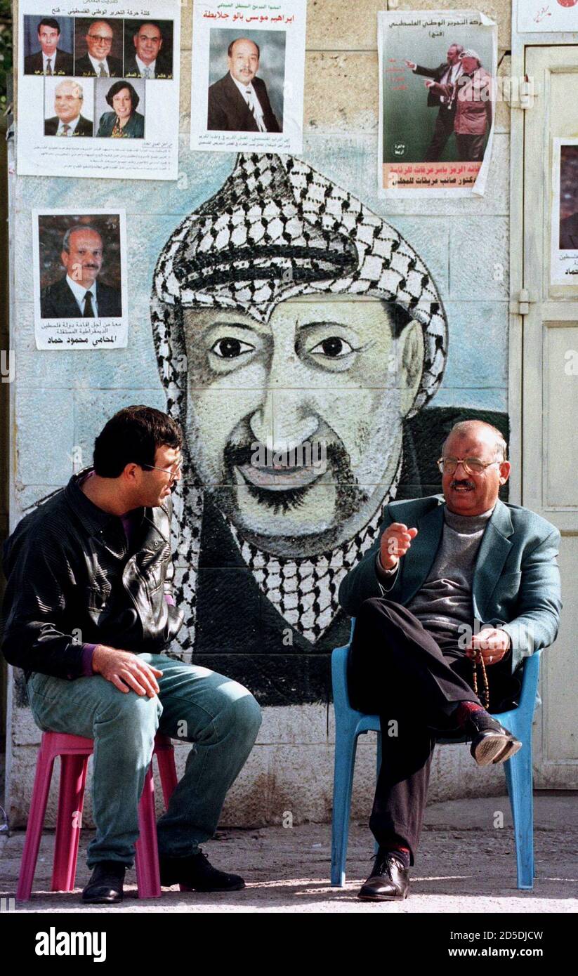 Palästinenser genießen das warme Wetter von Jericho, wie sie auf der Straße Januar 16 unter den Augen der PLO-Chef Yasser Arafat sitzen. Über Arafat sind einige Plakate, die Förderung der lokalen Kandidaten für nationalen Rates Sitze bei den bevorstehenden palästinensischen Wahlen 20 Januar stattfinden Stockfoto
