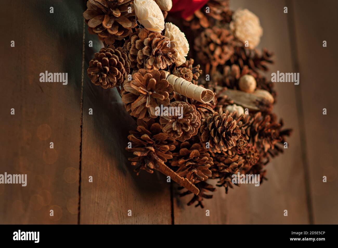 Auf einem hölzernen braunen Wandhintergrund mit verschwommenem Bokeh in einem dunklen Dachboden hängt ein Kranz von Händen von Kiefernzapfen, getrockneten Blumen, dekorative Elemente gemacht, Stockfoto