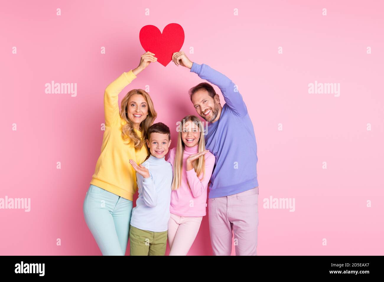 Foto von gemütlichen positiven Familie mit kleinen Kindern Mama Papa Halten Sie rote Papier Karte Herz isoliert über pastellfarbenen Hintergrund Stockfoto