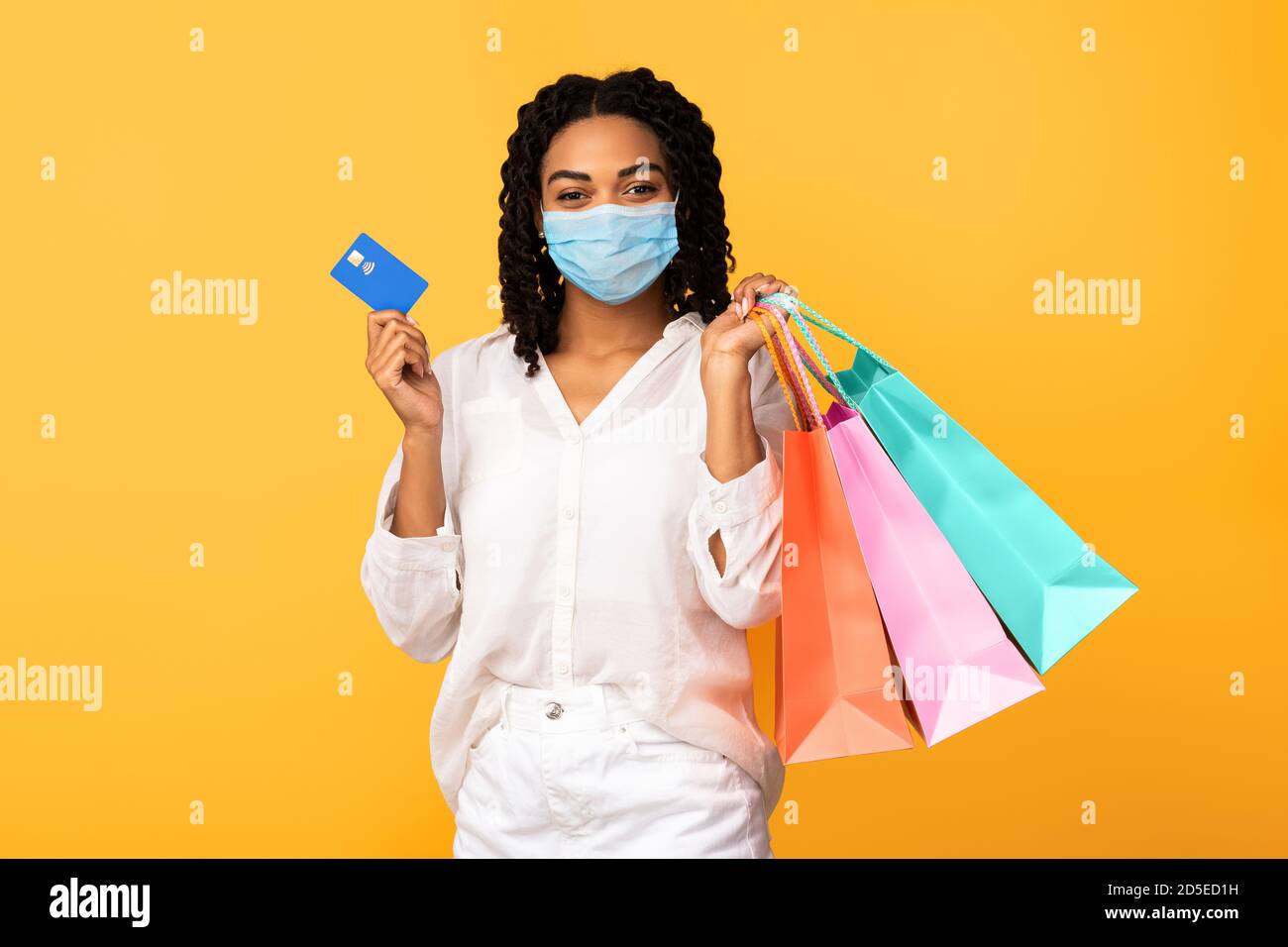 Lady In Maske Halten Kreditkarte Und Taschen, Gelber Hintergrund Stockfoto