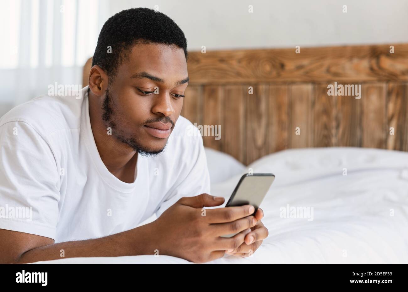 Ernsthafte Schwarze Mann Mit Handy Liegen Im Bett Drinnen Stockfoto