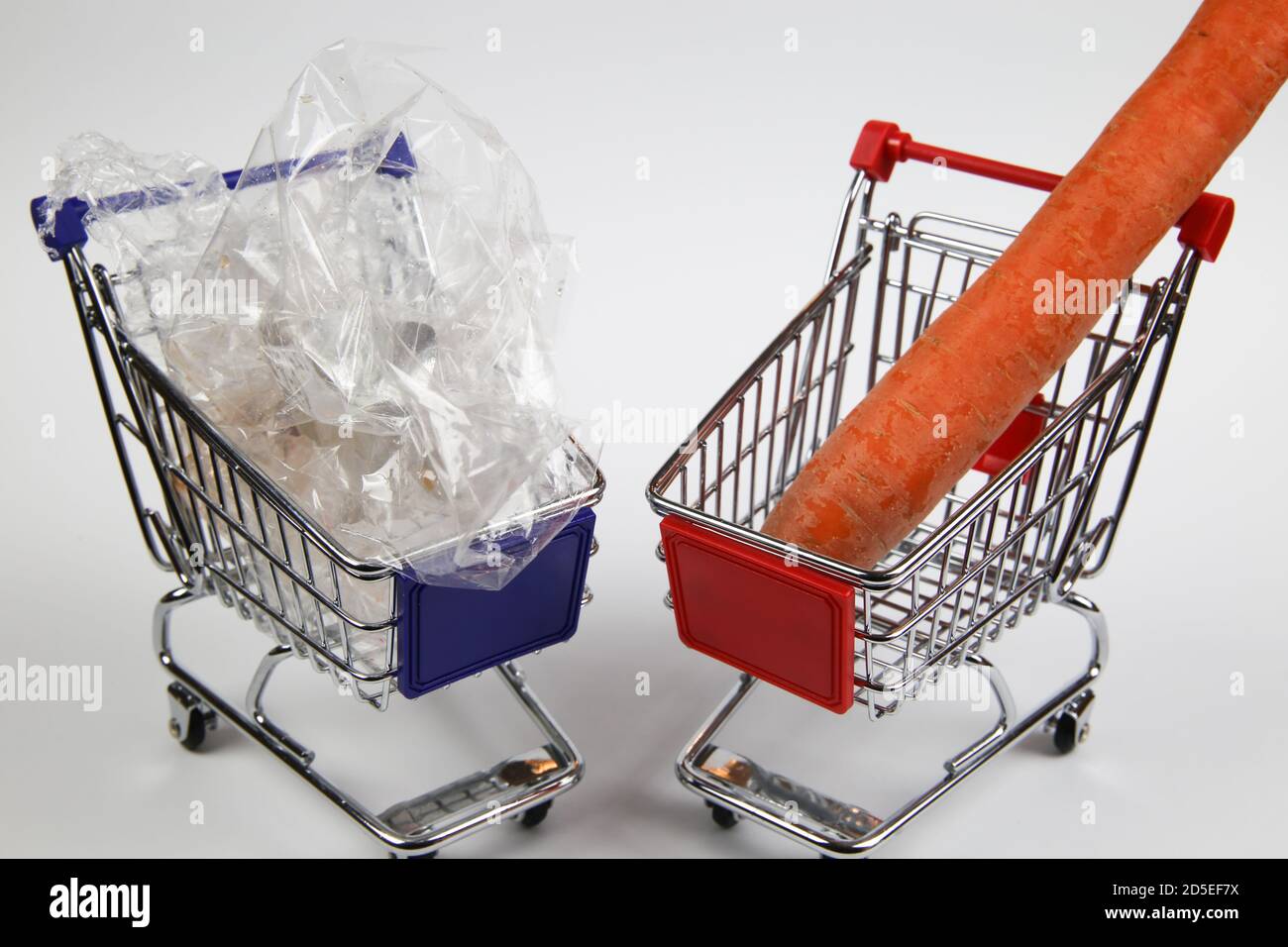 Blick auf zwei isolierte Warenkorb mit einem einzigen isoliert Karotten und zu viel Plastik-Verpackungsmüll Stockfoto