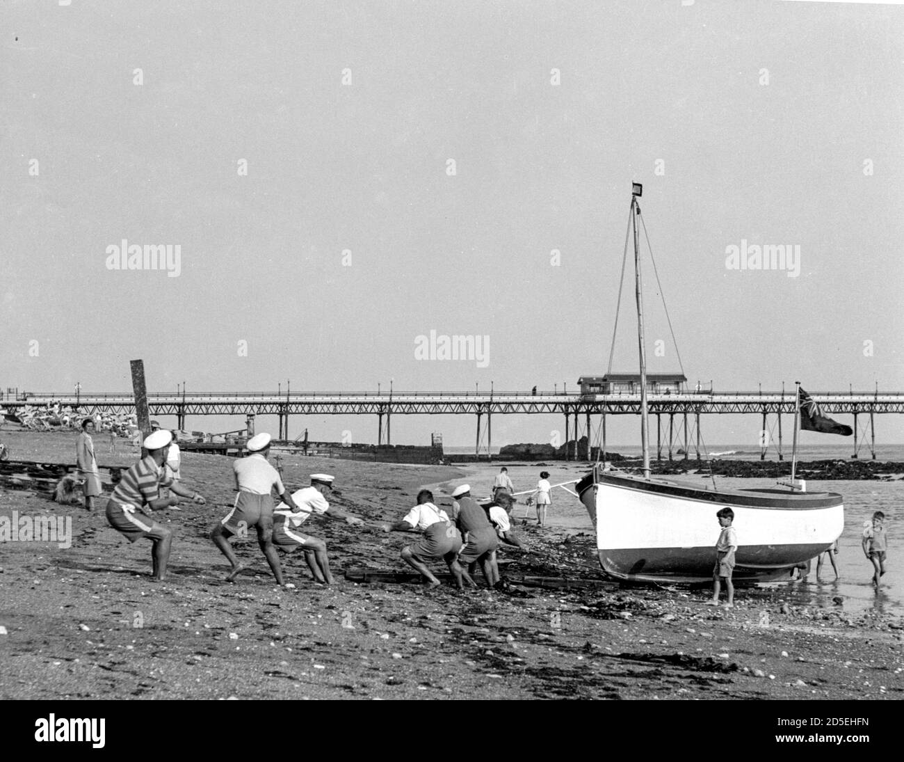 Eine Gruppe von Männern schleppen ihr Boot am Strand und aus dem Meer in Shanklin, Isle of Wight in den 1950er Jahren Stockfoto