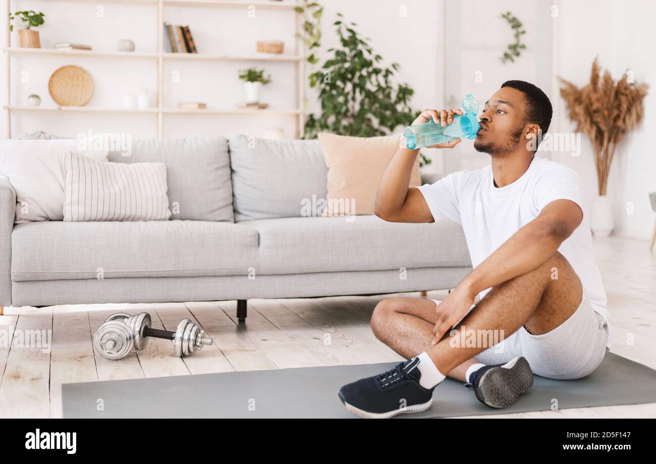 Schwarzer Mann Trinkwasser Während Des Trainings Sitzen Auf Matte Im Innen Stockfoto