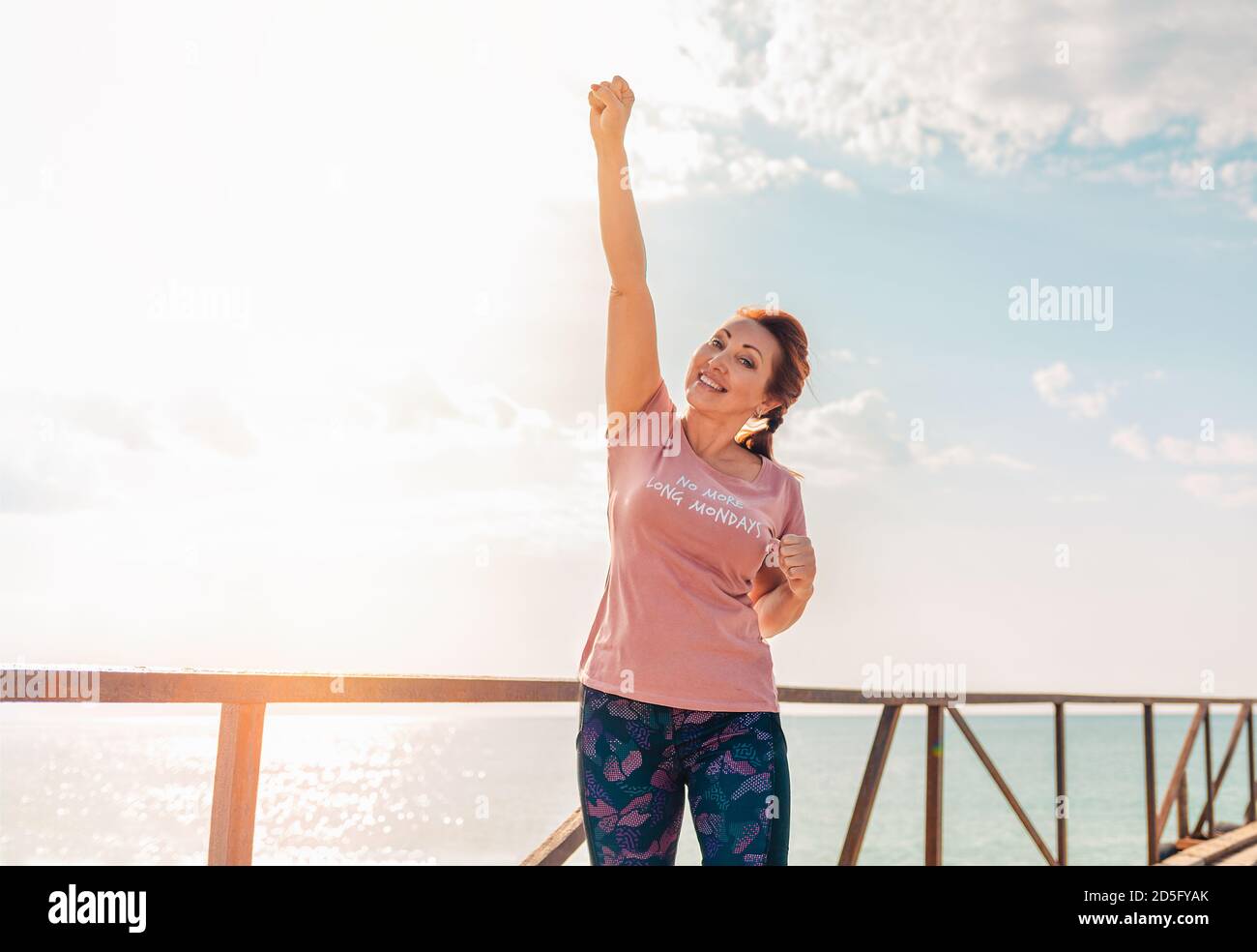 Eine Erwachsene Frau hebt ihre Hand glücklich hoch. Im Hintergrund der Himmel mit Wolken, sonniges Wetter. Speicherplatz kopieren. Konzept des menschlichen Ausdrucks. Stockfoto