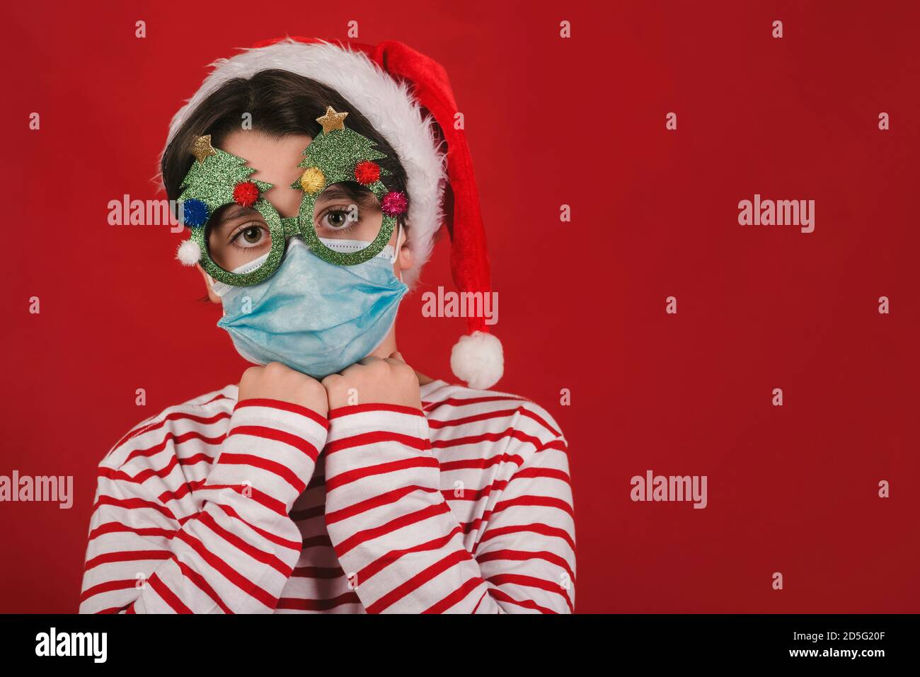 Frohe Weihnachten, Kind mit medizinischer Maske und lustige weihnachtsgläser auf rotem Hintergrund Stockfoto