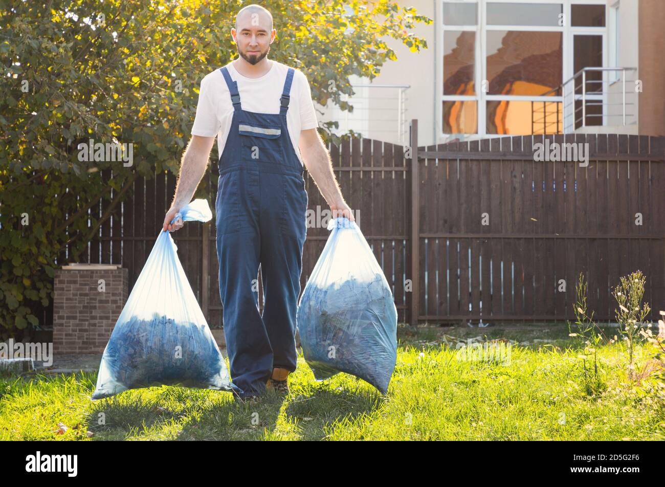 Der Gärtner lächelt und entfernt die Beutel mit Kompost. Blaue Uniform. Stockfoto