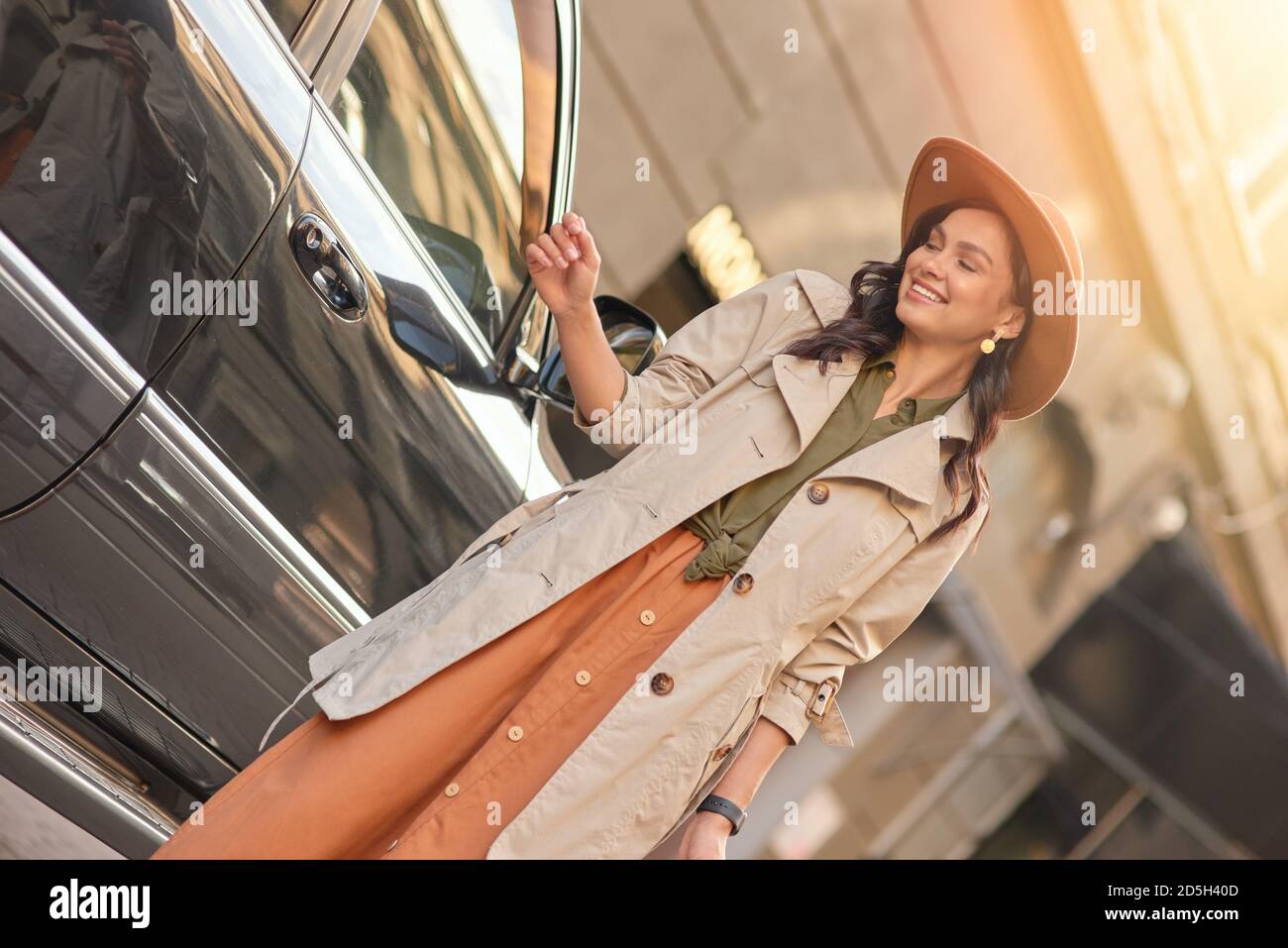 Junge glückliche stilvolle Frau mit Einkaufstaschen, die beiseite schauen und lächeln, während sie in der Nähe eines schwarzen Luxuswagens auf der Straße der Stadt steht. Menschen Lifestyle, Mode-Konzept Stockfoto