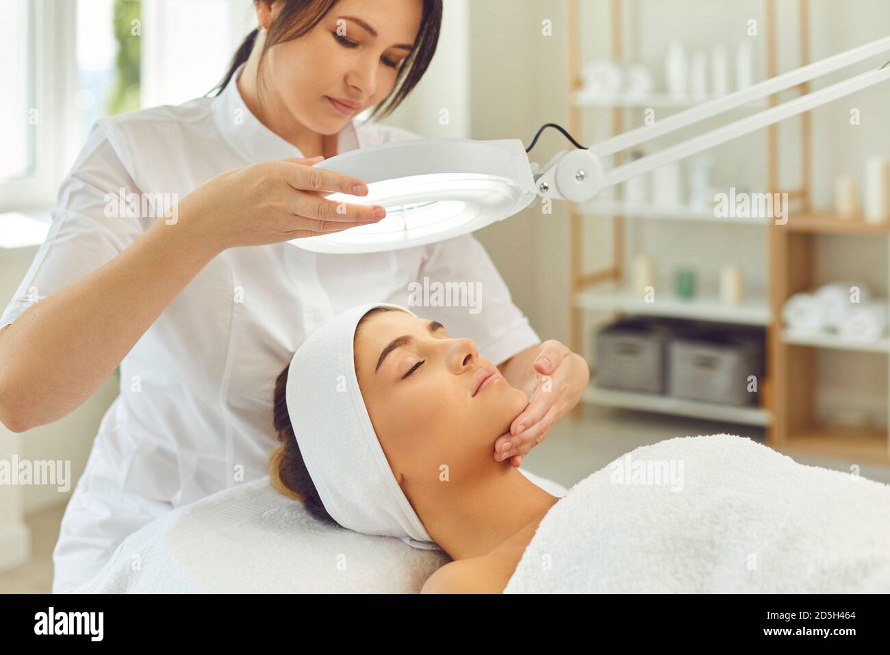 Frau Kosmetologe Blick auf heitere junge Frauen Gesicht anc Überprüfung Hautzustand Stockfoto
