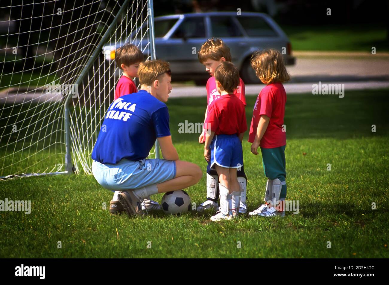 Coach unterrichtet junge Jungen und Mädchen das Spiel des Fußballs Und das Konzept der Teamarbeit Stockfoto