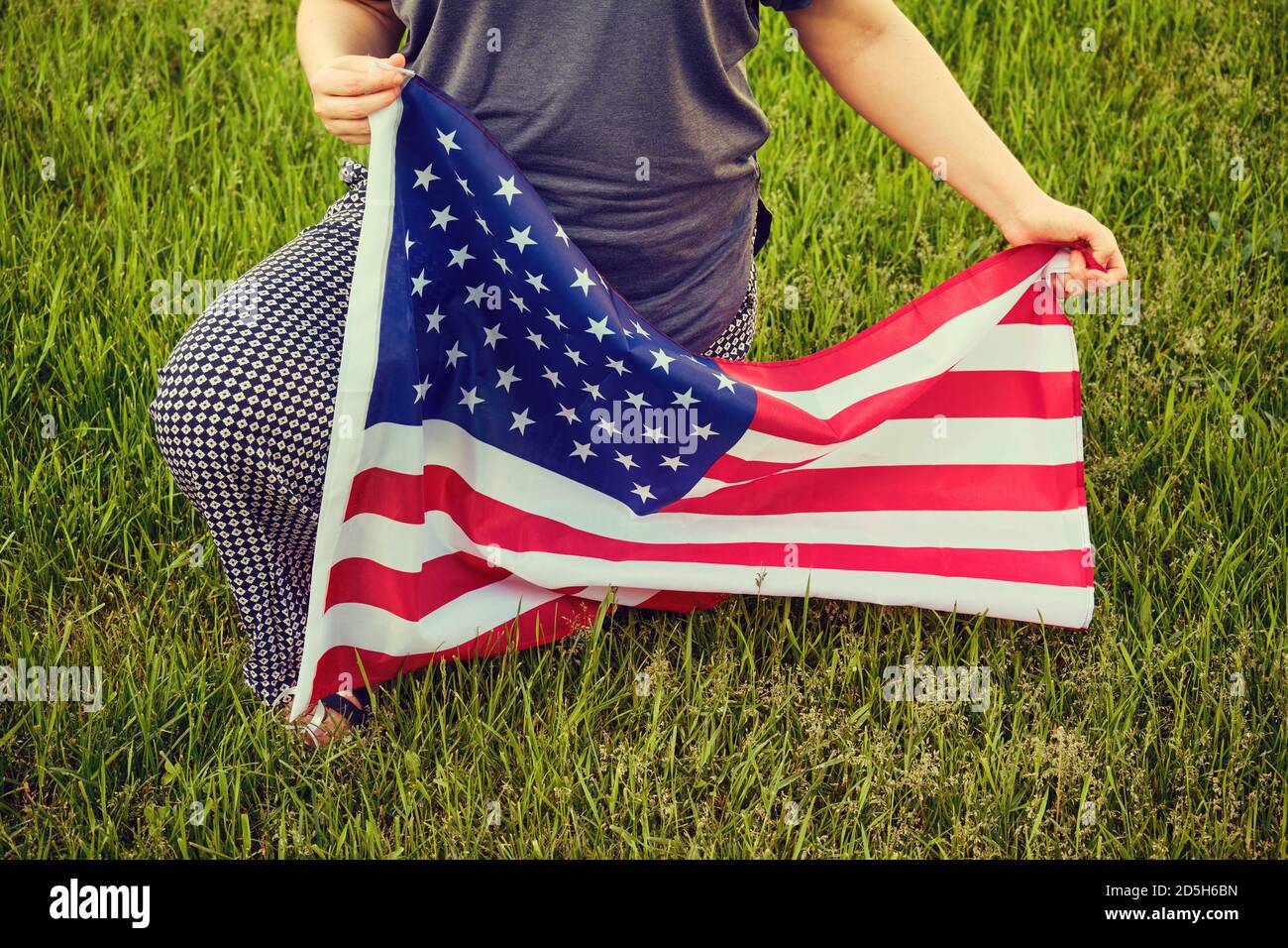 Protest im US-Park Gras, Frau kniet. USA Flagge, knieend auf grünem Hintergrund Stockfoto