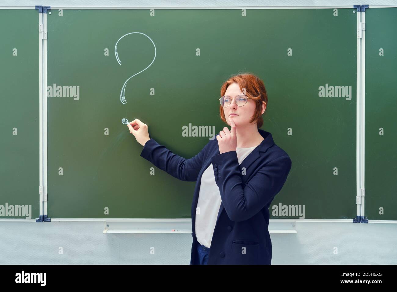Die Lehrerin steht an der Tafel mit einem mit Kreide gezeichneten Fragezeichen. Die Lehrerin steht mit einem nachdenklichen Gesicht Stockfoto
