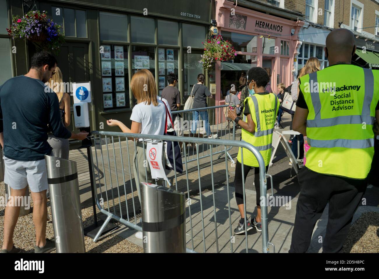 Soziale Distanzberater helfen Besuchern des Broadway Market, mit Straßenschildern, die darauf hinweisen, dass die soziale Distanz aufgrund der Coronavirus / Covid-19 Pandemie in Hackney, London, England, Großbritannien, geschützt ist Stockfoto