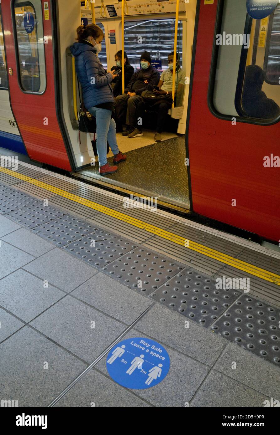 Passagiere auf einer Londoner U-Bahn-Station, mit Schildern, die darauf hinweisen, dass die soziale Distanz wegen Coronavirus / Covid-19 Pandemie in London, England, Großbritannien, zu halten Stockfoto