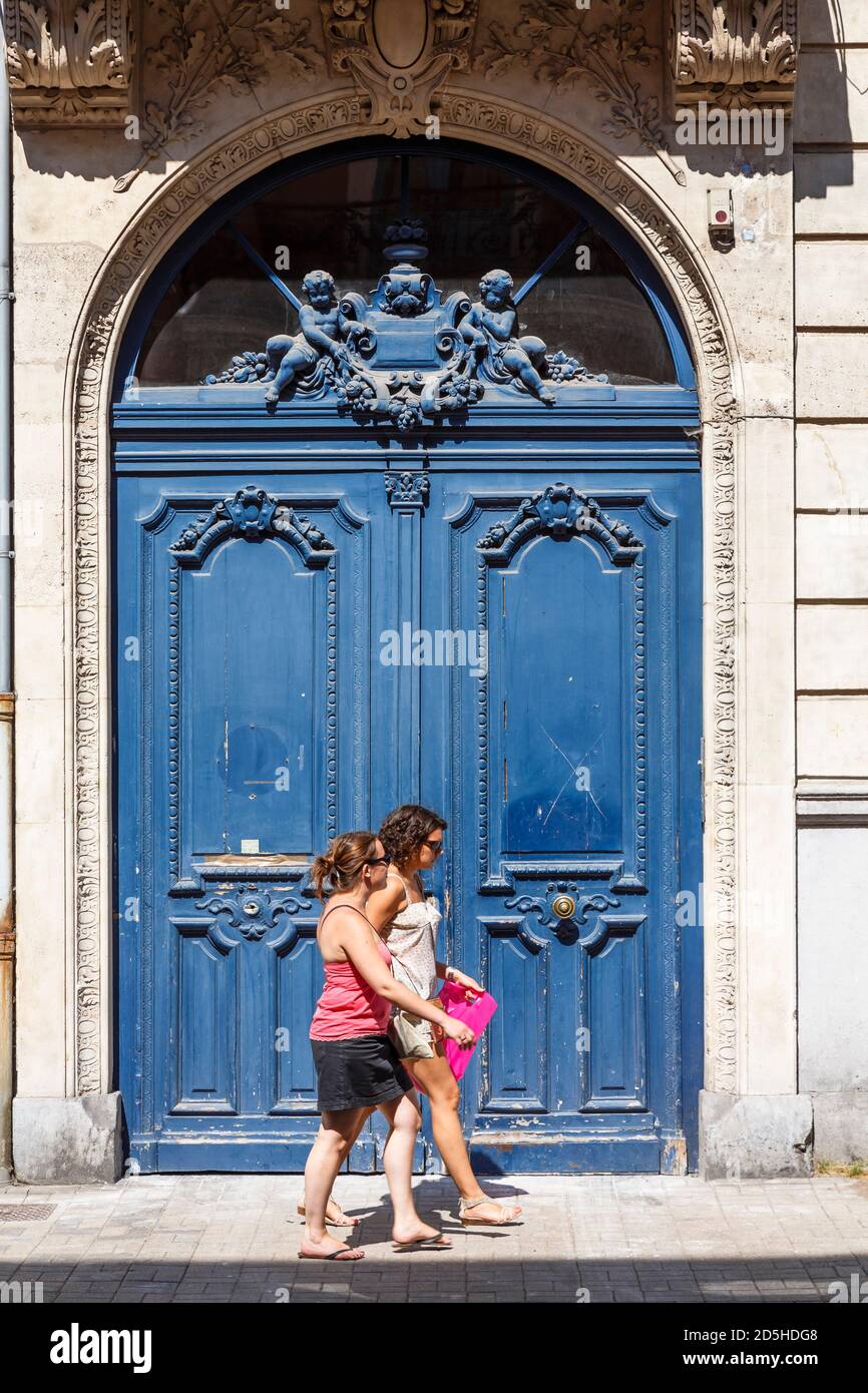 LILLE, FRANKREICH - 19. Juli 2013. Zwei junge Frauen passieren eine alte verblasste blaue Tür in einem gewölbten Eingang, Lille Street Scene Stockfoto