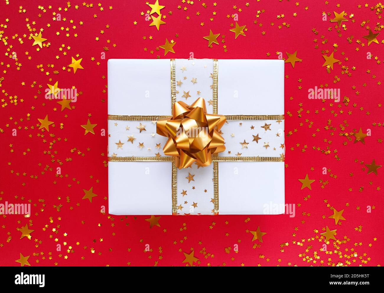 Weiße Geschenkbox mit goldener Schleife und Sternen auf rotem Hintergrund. Stockfoto