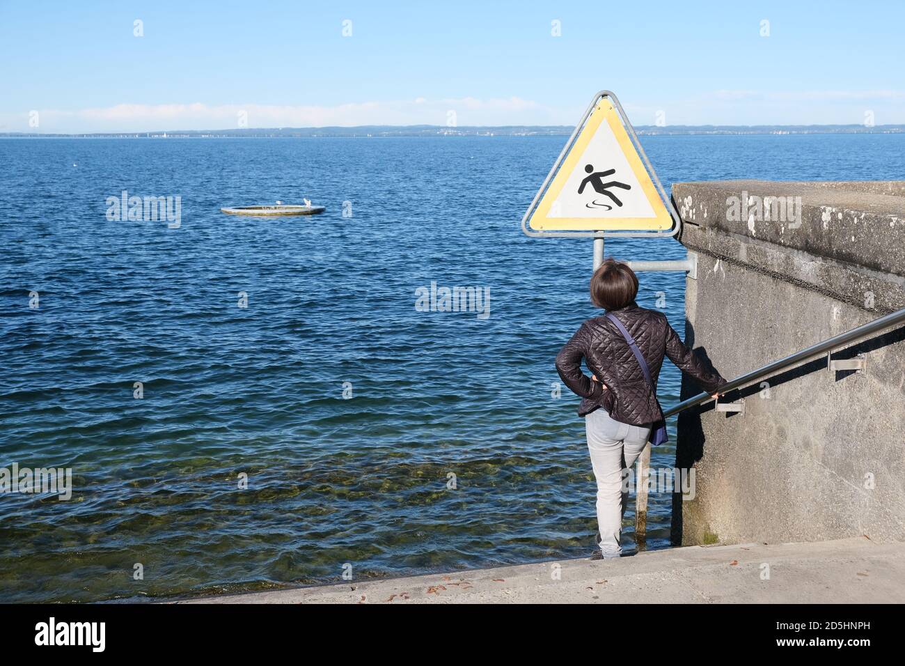 Weibliche stehend auf der Treppe zum See unter dem schild „Vorsicht“ Stockfoto