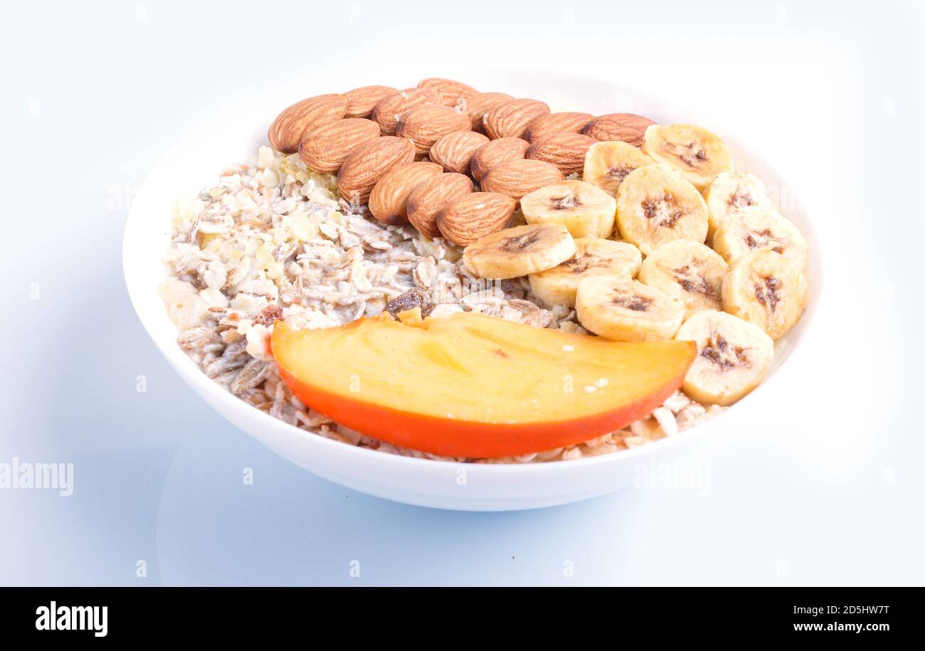 Ein Teller mit Müsli, Mandeln, Banane, Kaki isoliert auf weißem Hintergrund. Nahaufnahme. Stockfoto
